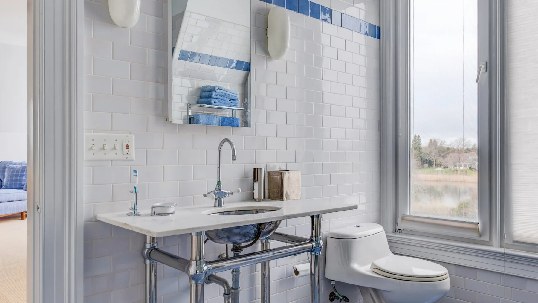 Un baño luminoso con lavabo alicatado e inodoro junto a una ventana grande.