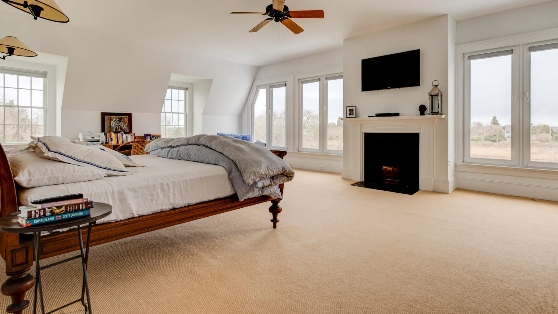 Un dormitorio luminoso con una cama, una chimenea y grandes ventanas.