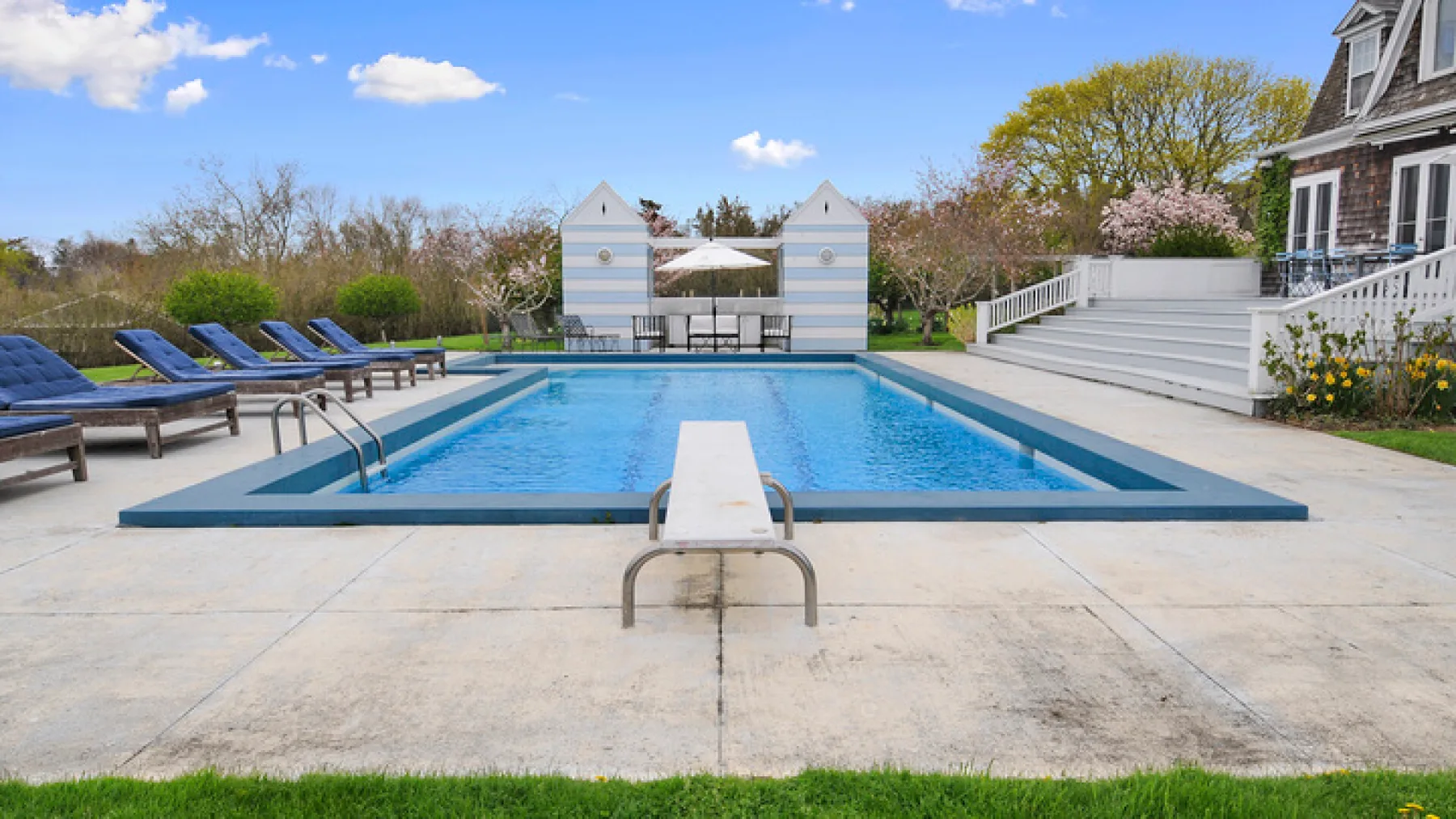 Una piscina al aire libre con asientos reclinables y un trampolín.
