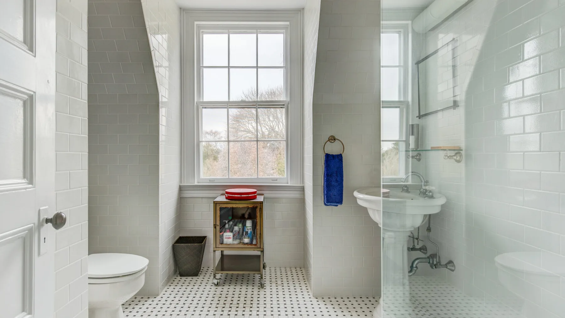 Un baño luminoso con una ventana, lavabo de pedestal, inodoro y ducha de vidrio.