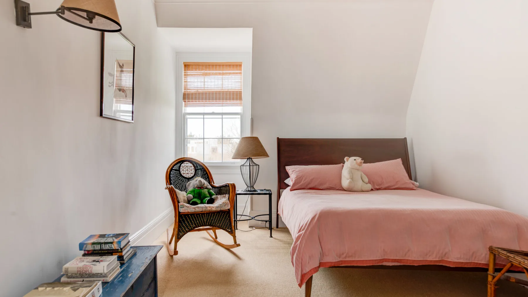 Un dormitorio con una cama vestida con ropa de cama rosa y una silla de mimbre junto a la ventana.