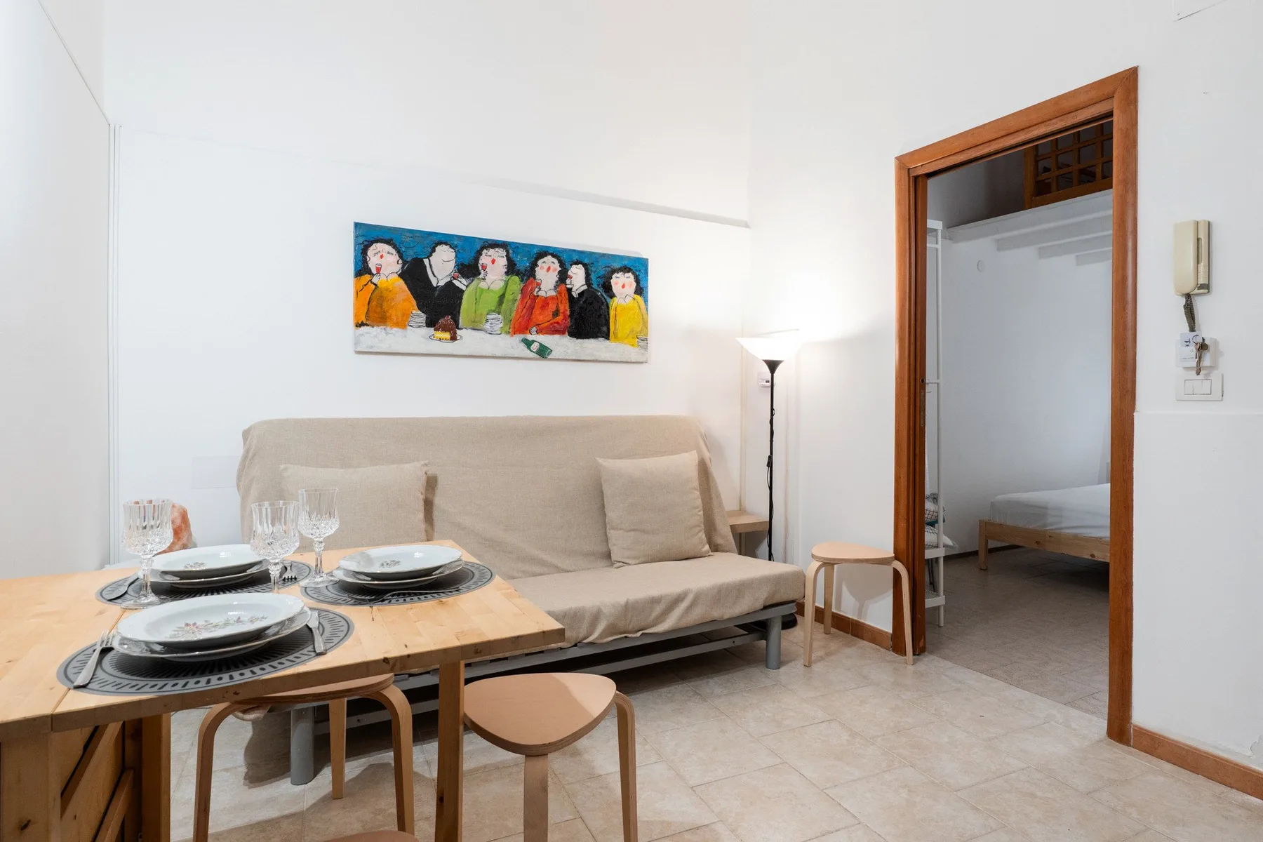 Una pequeña sala tiene una mesa de comedor frente a un sofá y una puerta abierta.