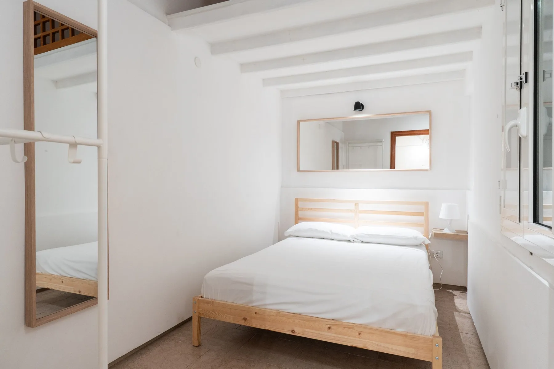 Un dormitorio luminoso con una cama de madera y un espejo grande en la pared.