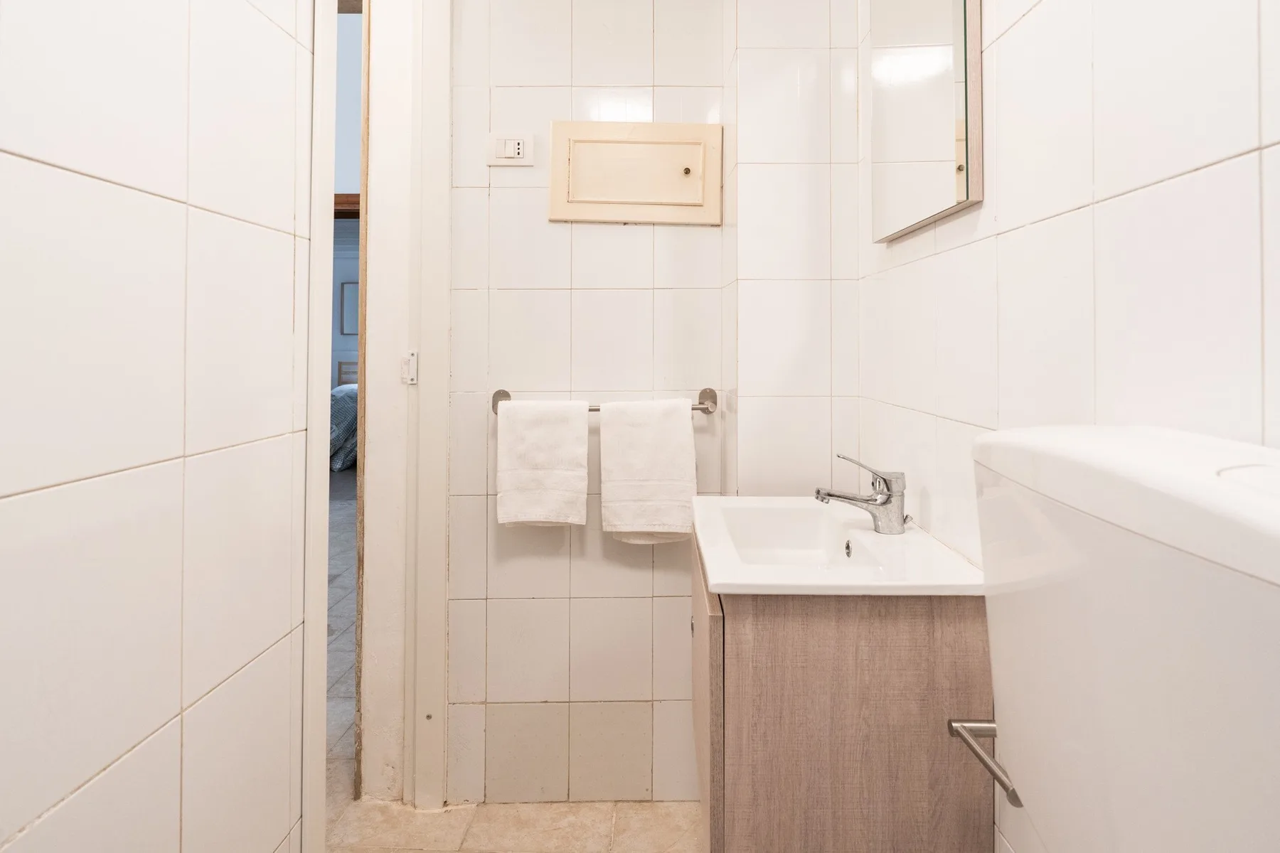 Un baño alicatado con lavabo, espejo y toallas colgadas en una barra.