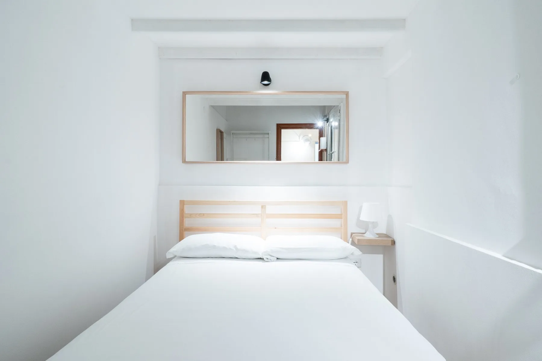 Un dormitorio luminoso con una cama bien tendida bajo un espejo de pared.