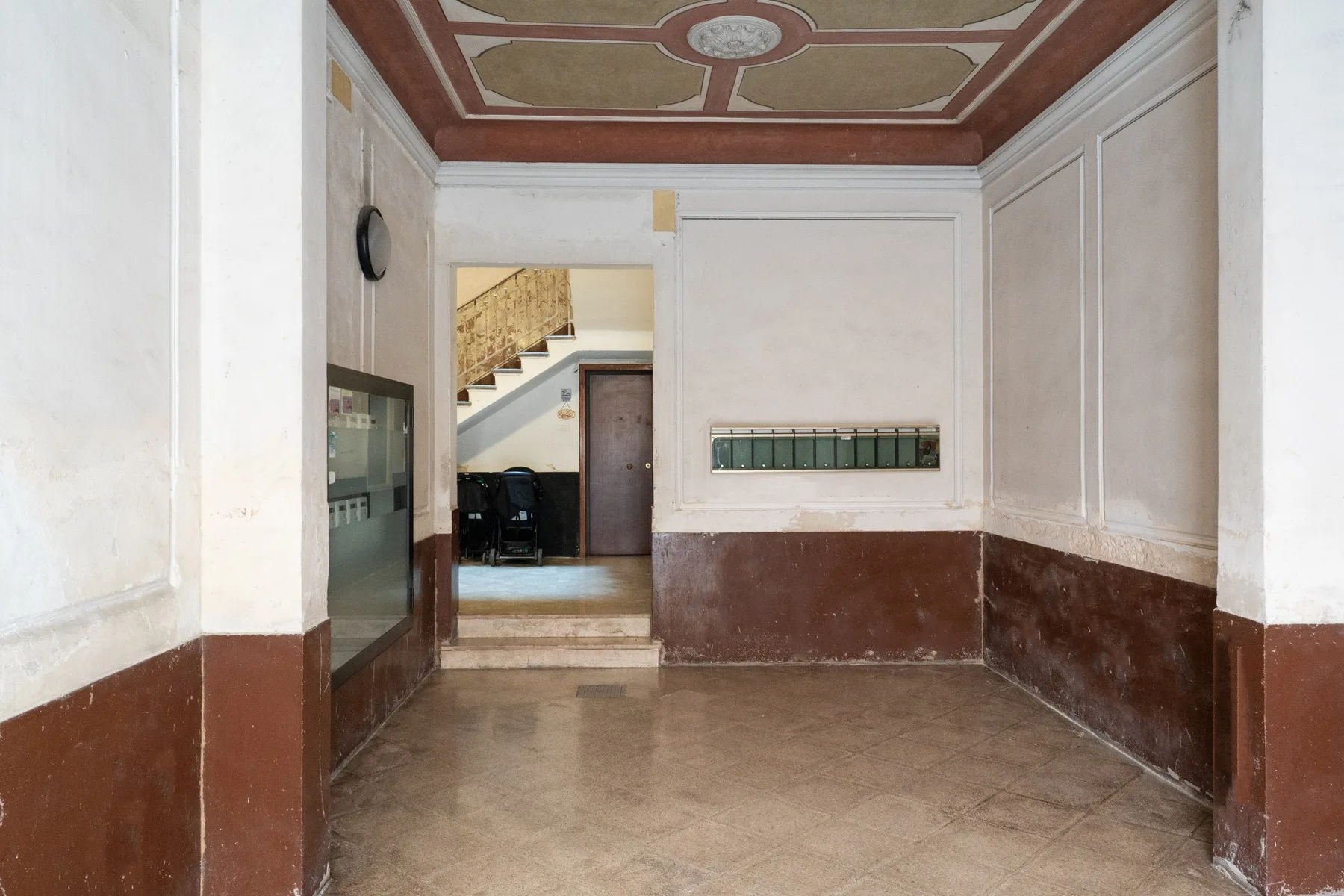 Un pasillo interior alargado tiene paredes claras, molduras inferiores oscuras y un techo decorado.