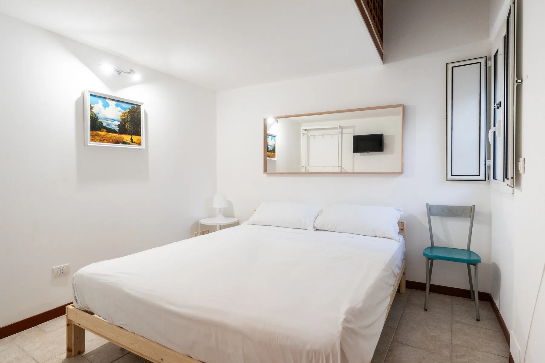 Un dormitorio luminoso con una cama bajo un espejo de pared.