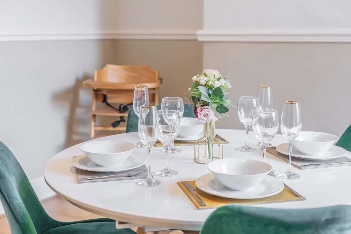 Una mesa de comedor está puesta con vajilla blanca, cristalería y un centro floral.