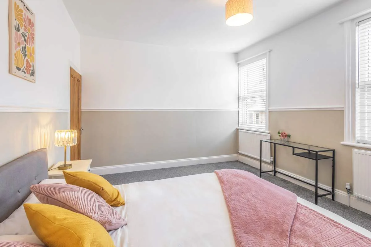 Un dormitorio con una cama, una lámpara de noche y una consola.