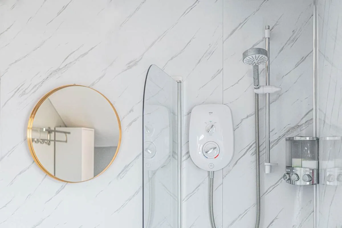 Pared de baño con diseño marmolado, espejo redondo y accesorios de ducha.
