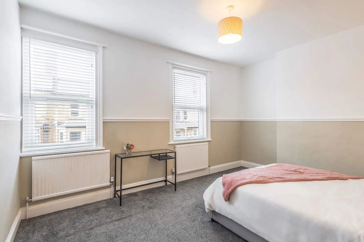 Un dormitorio con una cama, dos ventanas y una mesa pequeña.