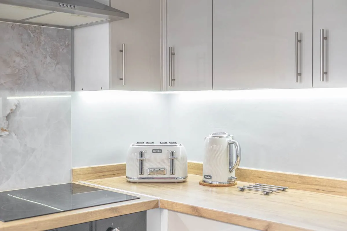 Una encimera de cocina con una tostadora y un hervidor eléctrico bajo armarios blancos.