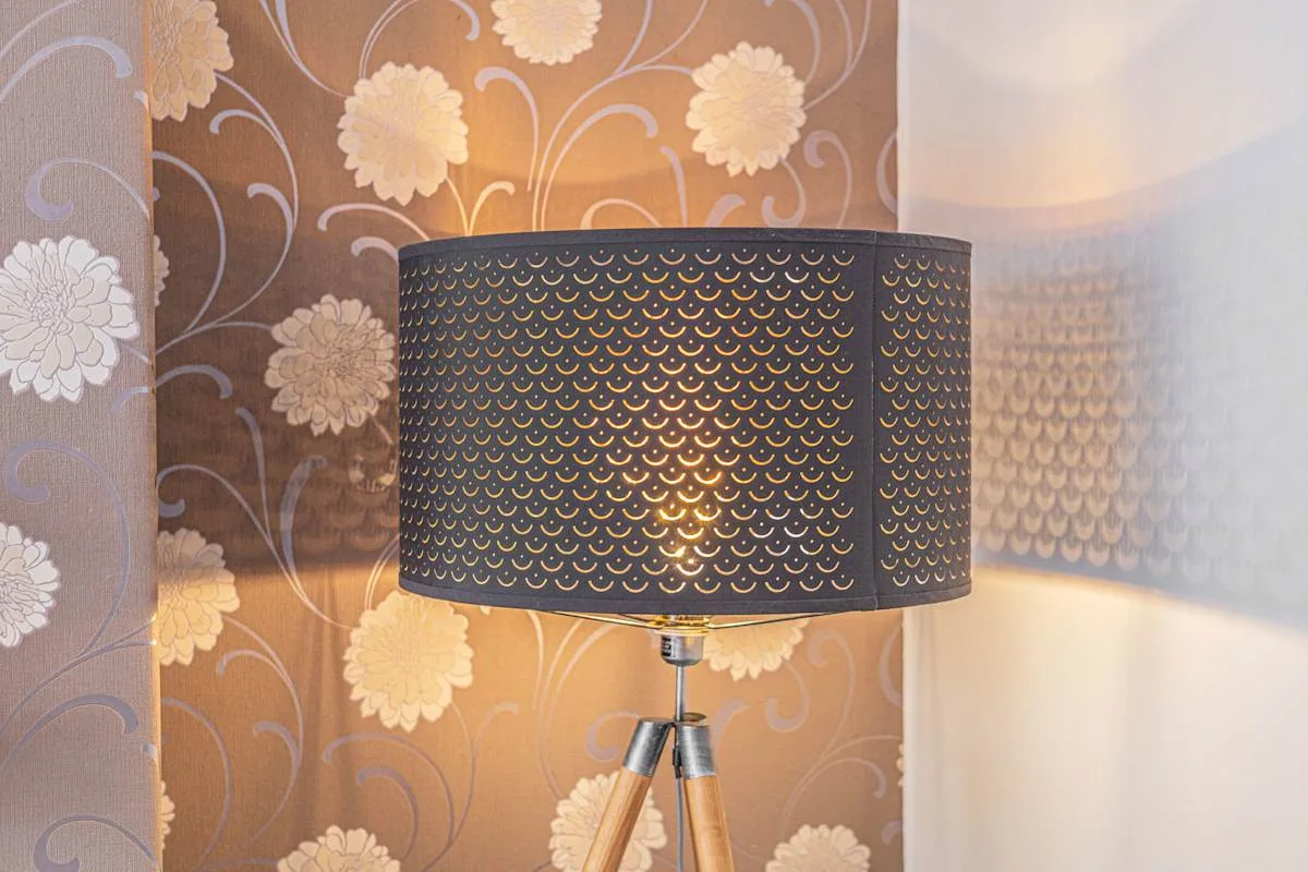 Una lámpara de pie está frente a un papel pintado floral en una habitación con luz tenue.