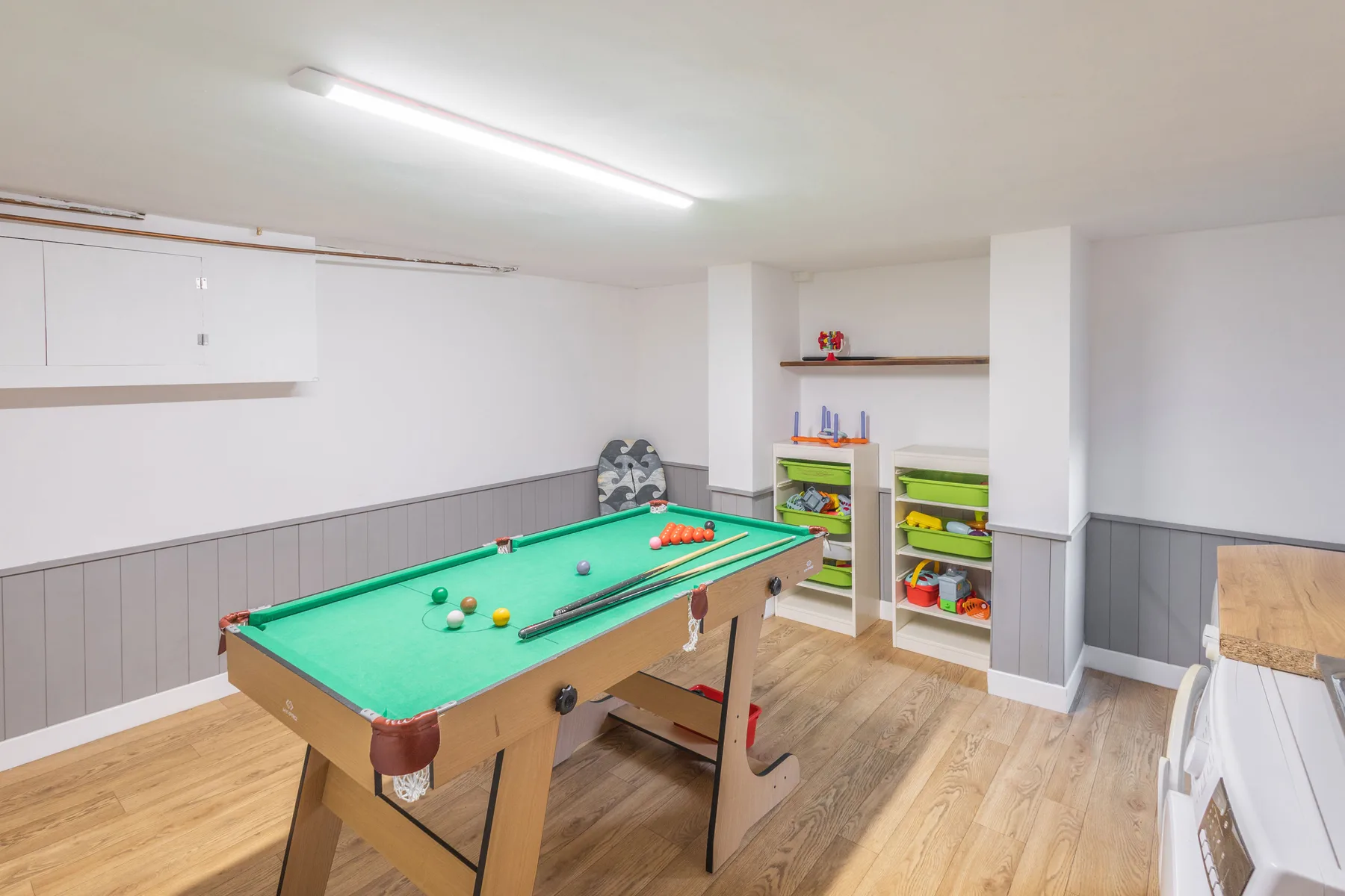 Sala de juegos con una mesa de billar de paño verde y estantes de almacenamiento.