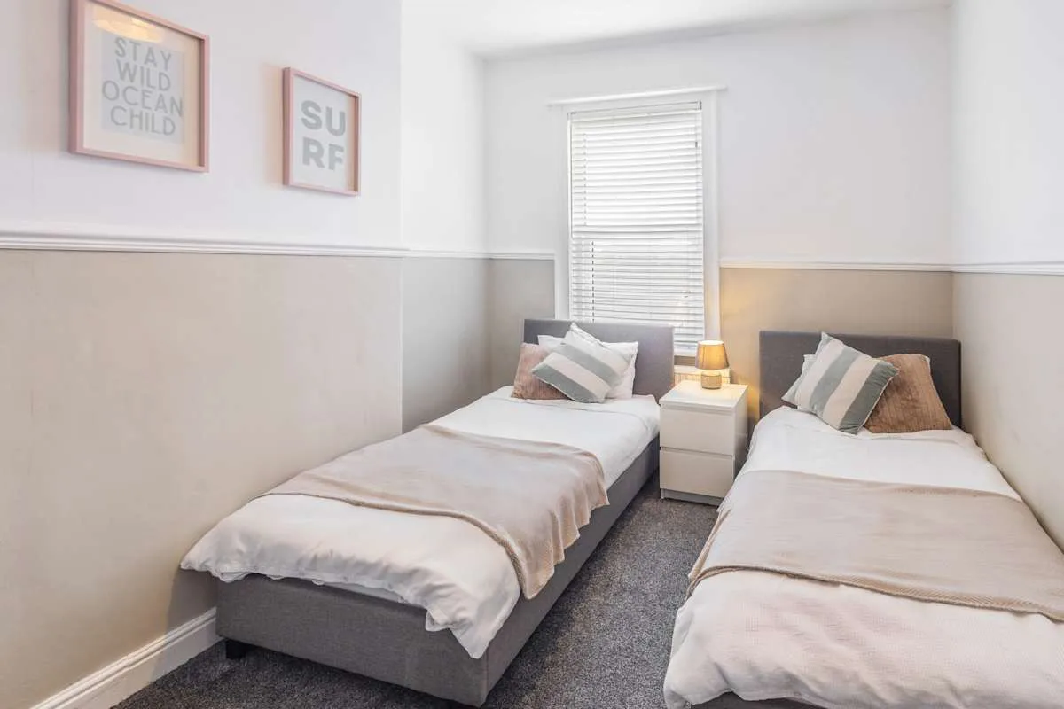 Un dormitorio luminoso con dos camas individuales bajo una ventana.