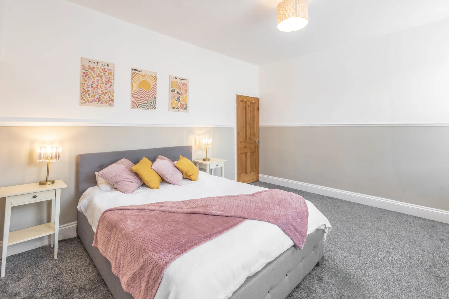 Un dormitorio con una cama vestida con ropa de cama blanca y una manta rosa.