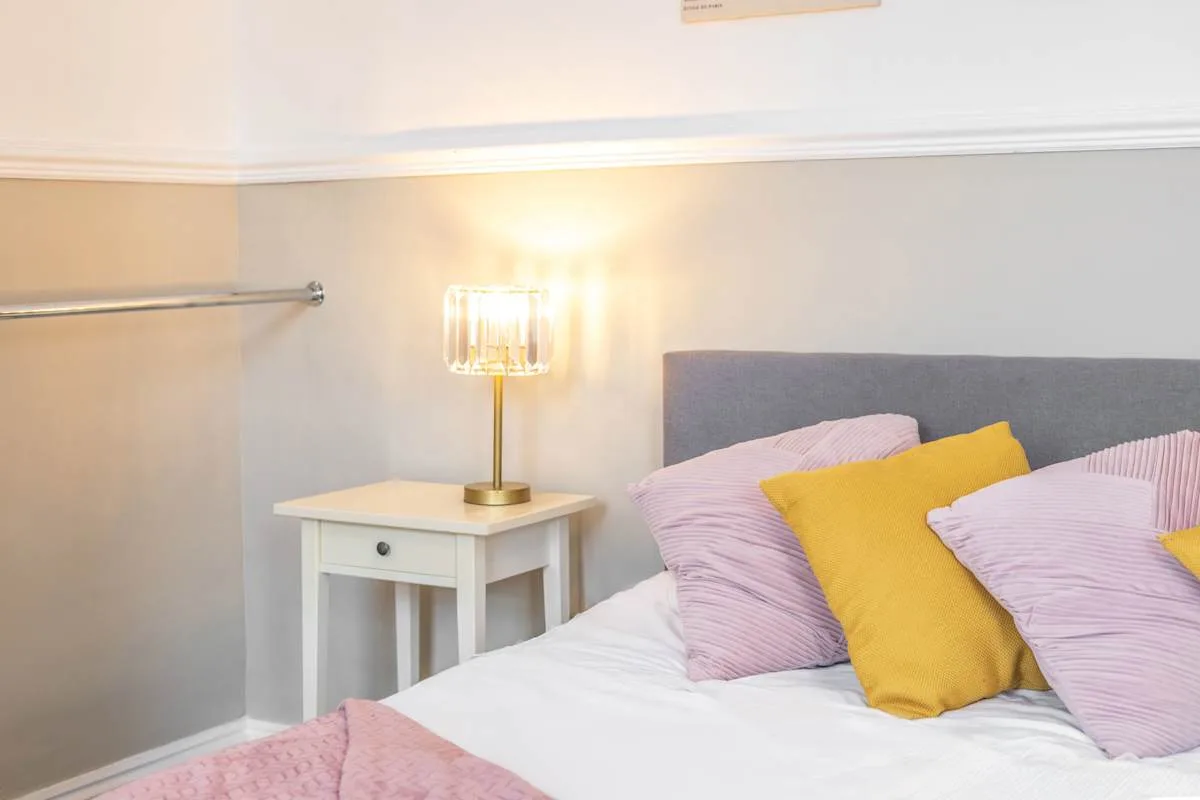 Dormitorio con cama, cojín amarillo y lámpara de mesita.