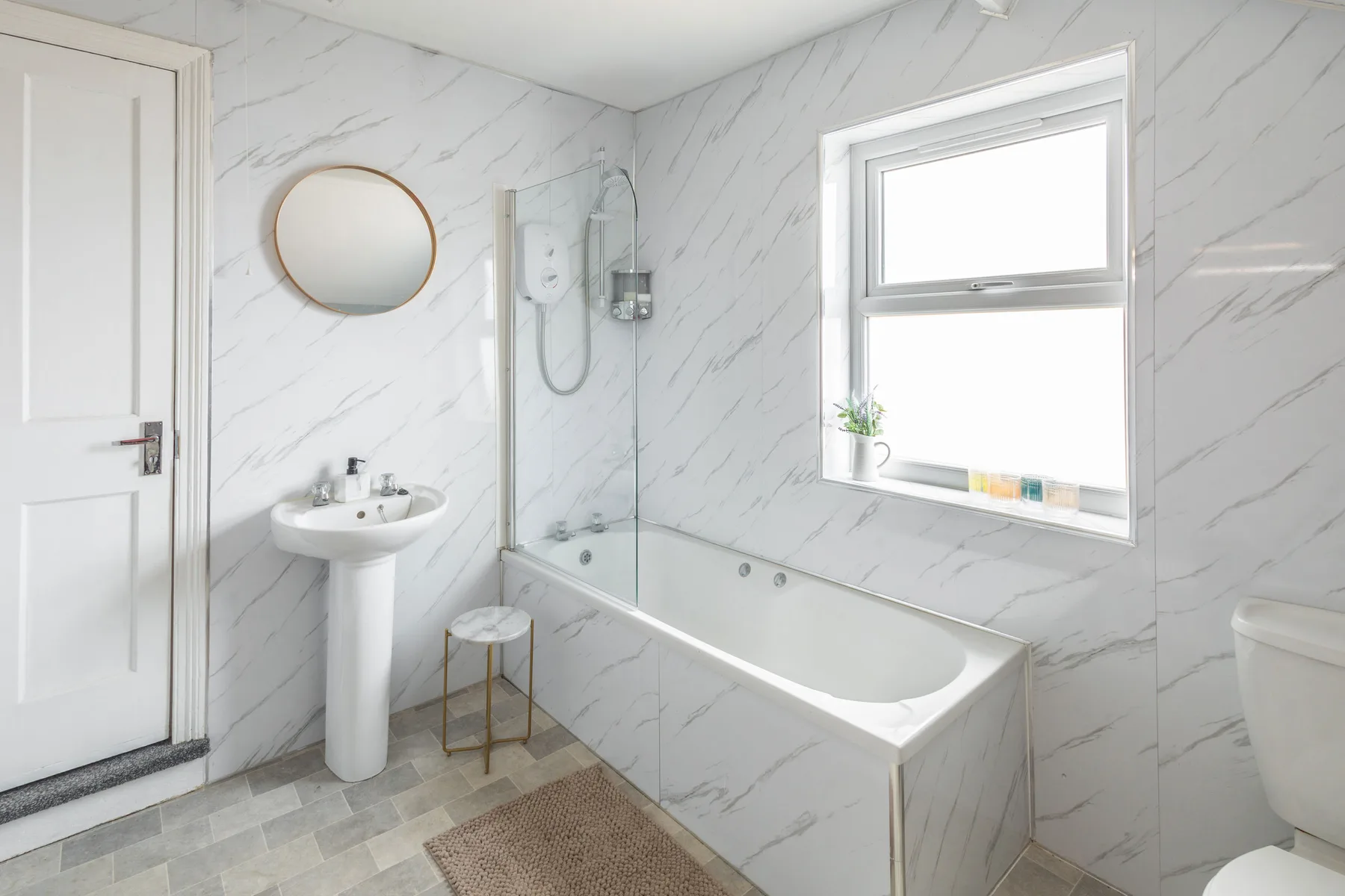 A bright bathroom with a bathtub, glass shower screen, and pedestal sink.