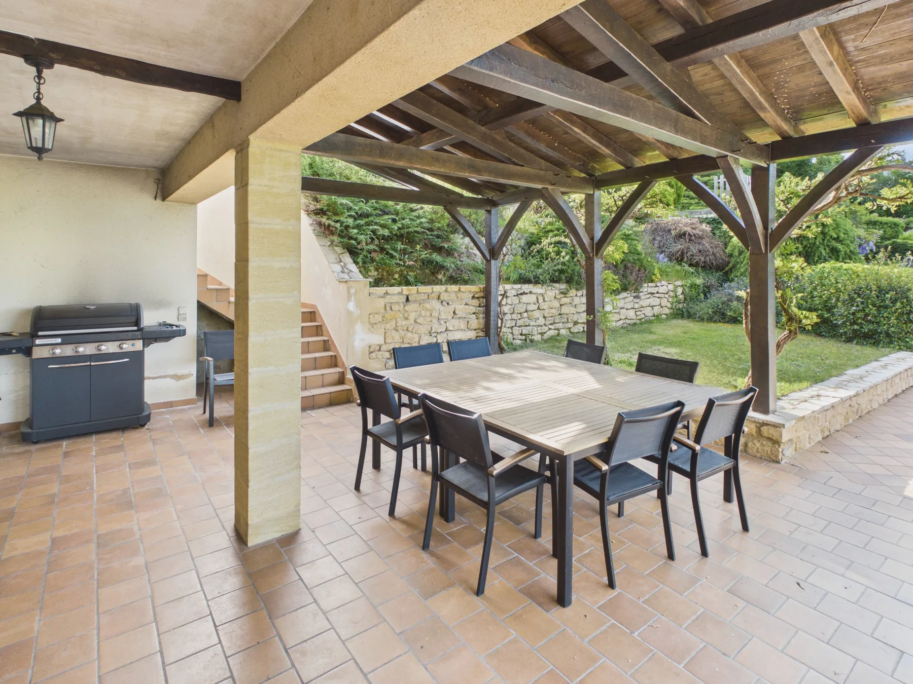 Comedor exterior cubierto con una mesa y sillas junto a un jardín.