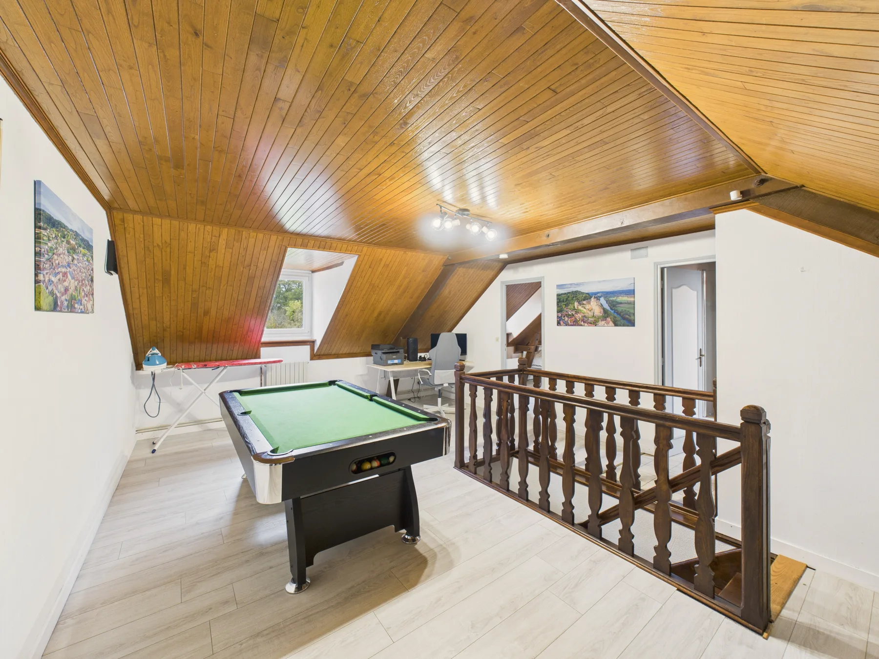Una sala de juegos con una mesa de billar bajo un techo inclinado de madera.