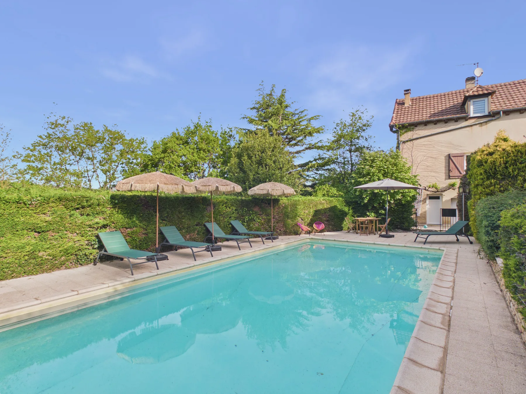 Piscina al aire libre junto a una casa, con asientos y vegetación.