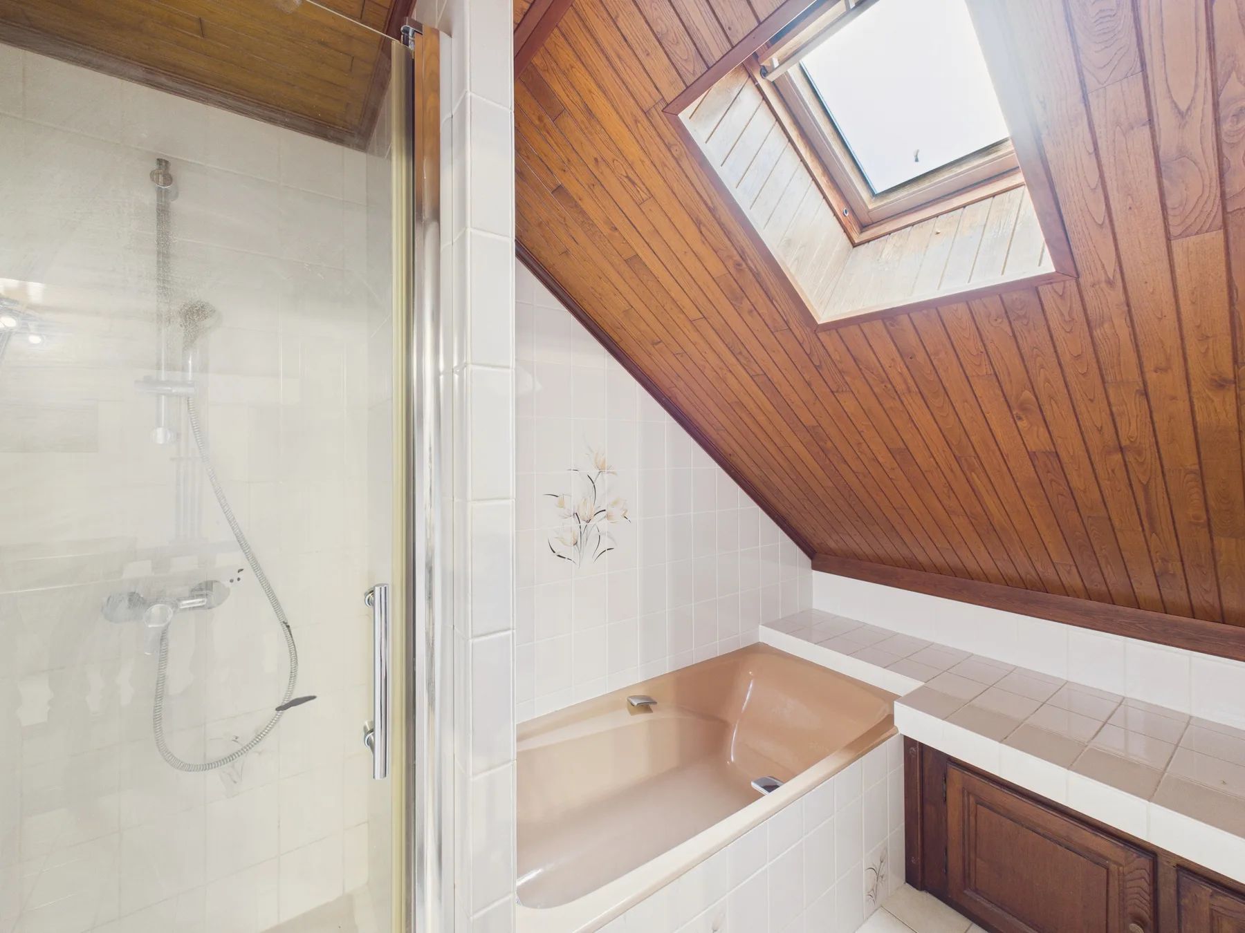 Un baño con bañera, ducha y techo inclinado de madera.