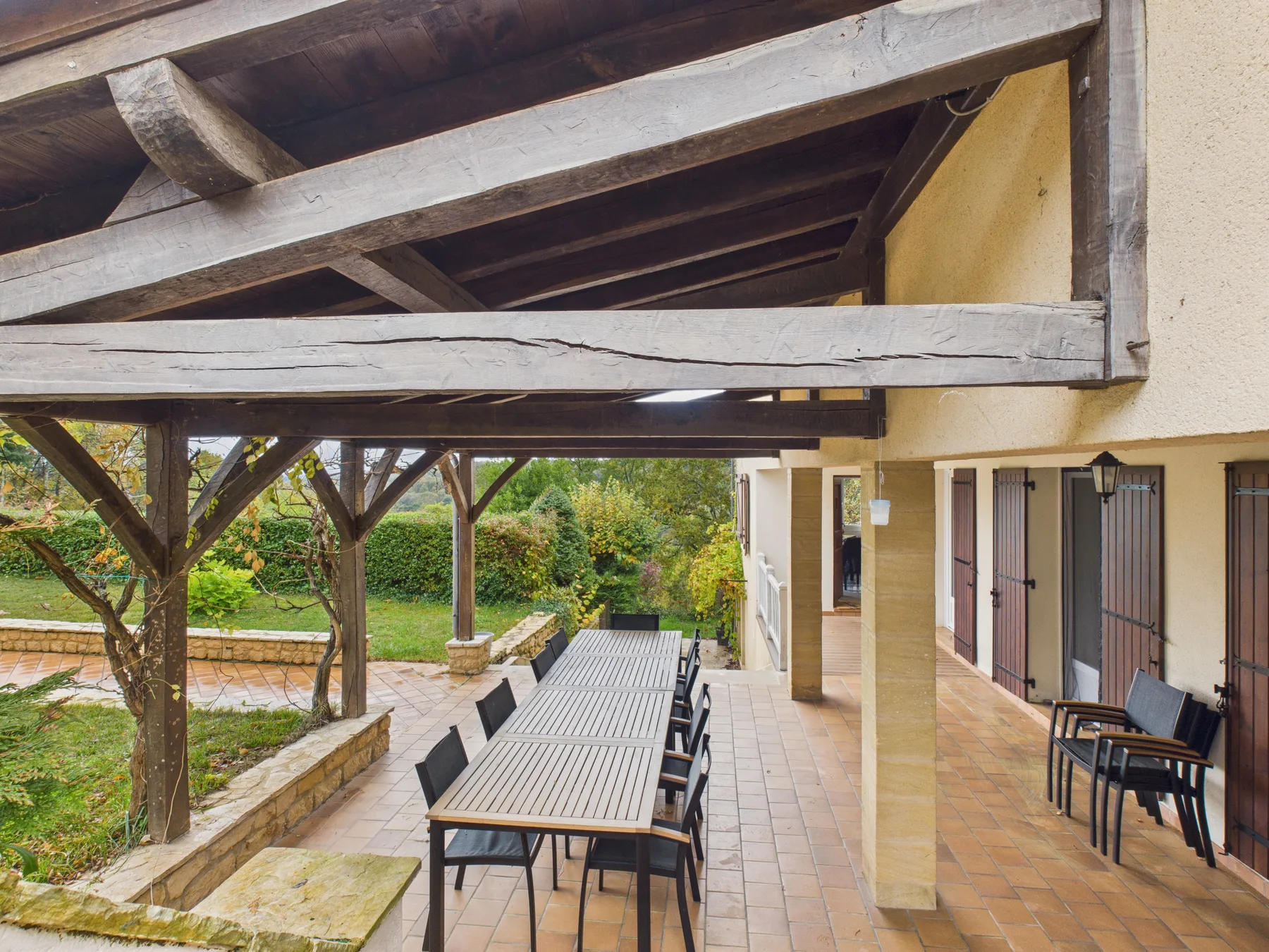 Comedor exterior cubierto con una mesa larga junto al jardín.