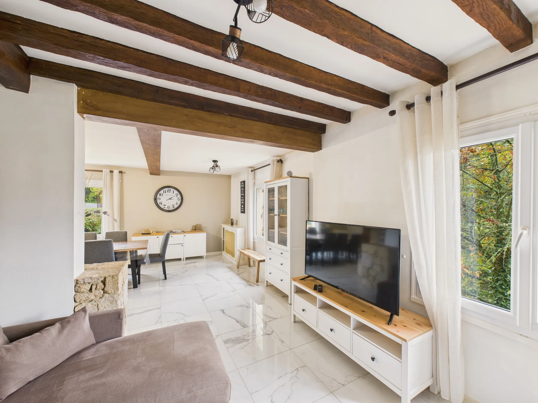 Una sala de estar y comedor luminosa con vigas a la vista y grandes ventanas.