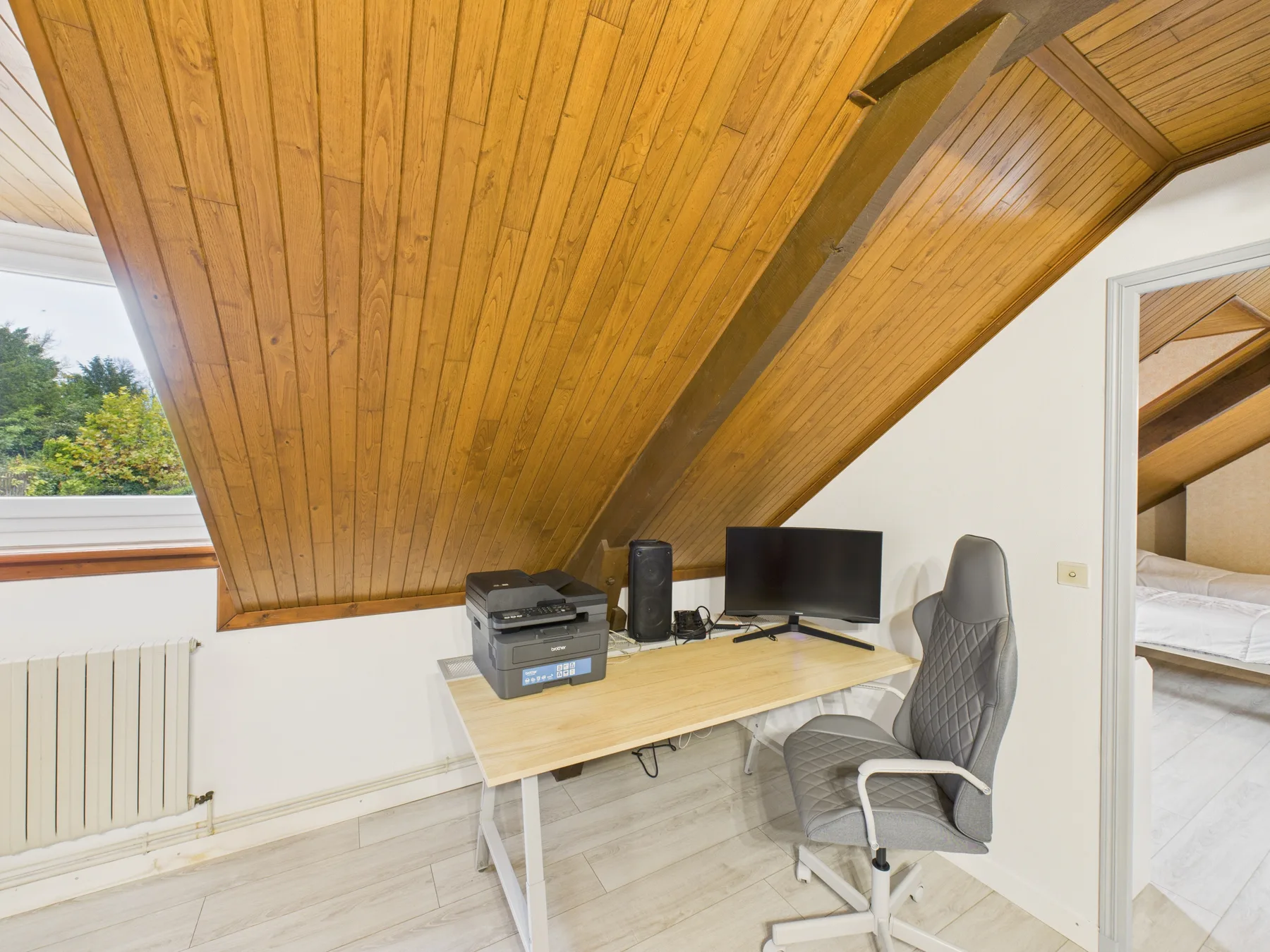 Un escritorio con computadora y silla está bajo un techo de madera inclinado.