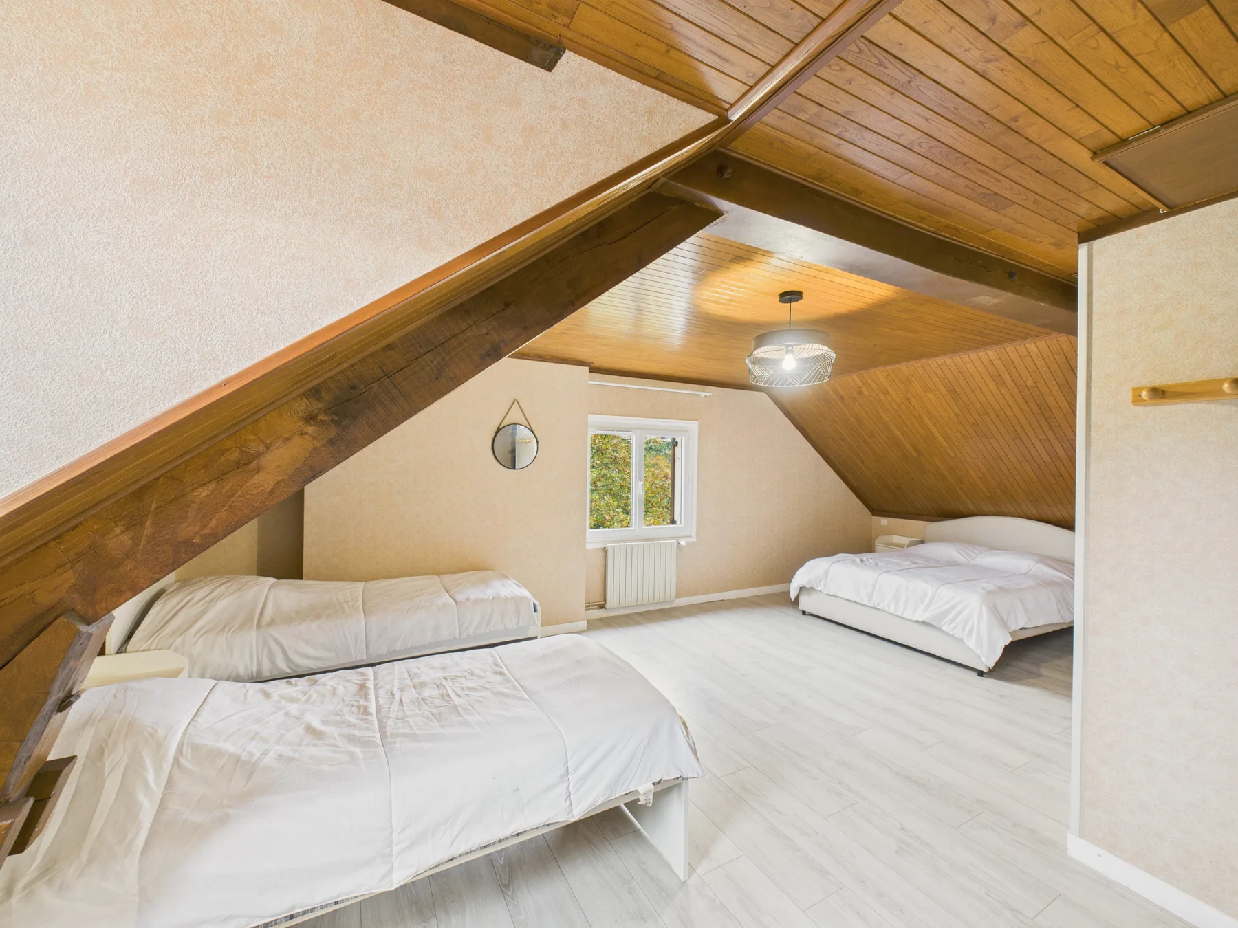 Un dormitorio con camas bajo un techo de madera inclinado y una ventana.