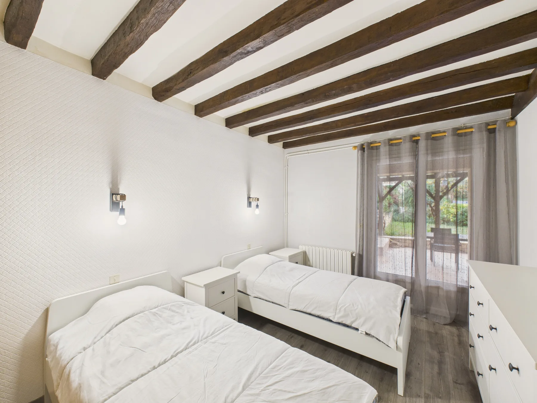 Un dormitorio luminoso con dos camas y vigas expuestas en el techo.