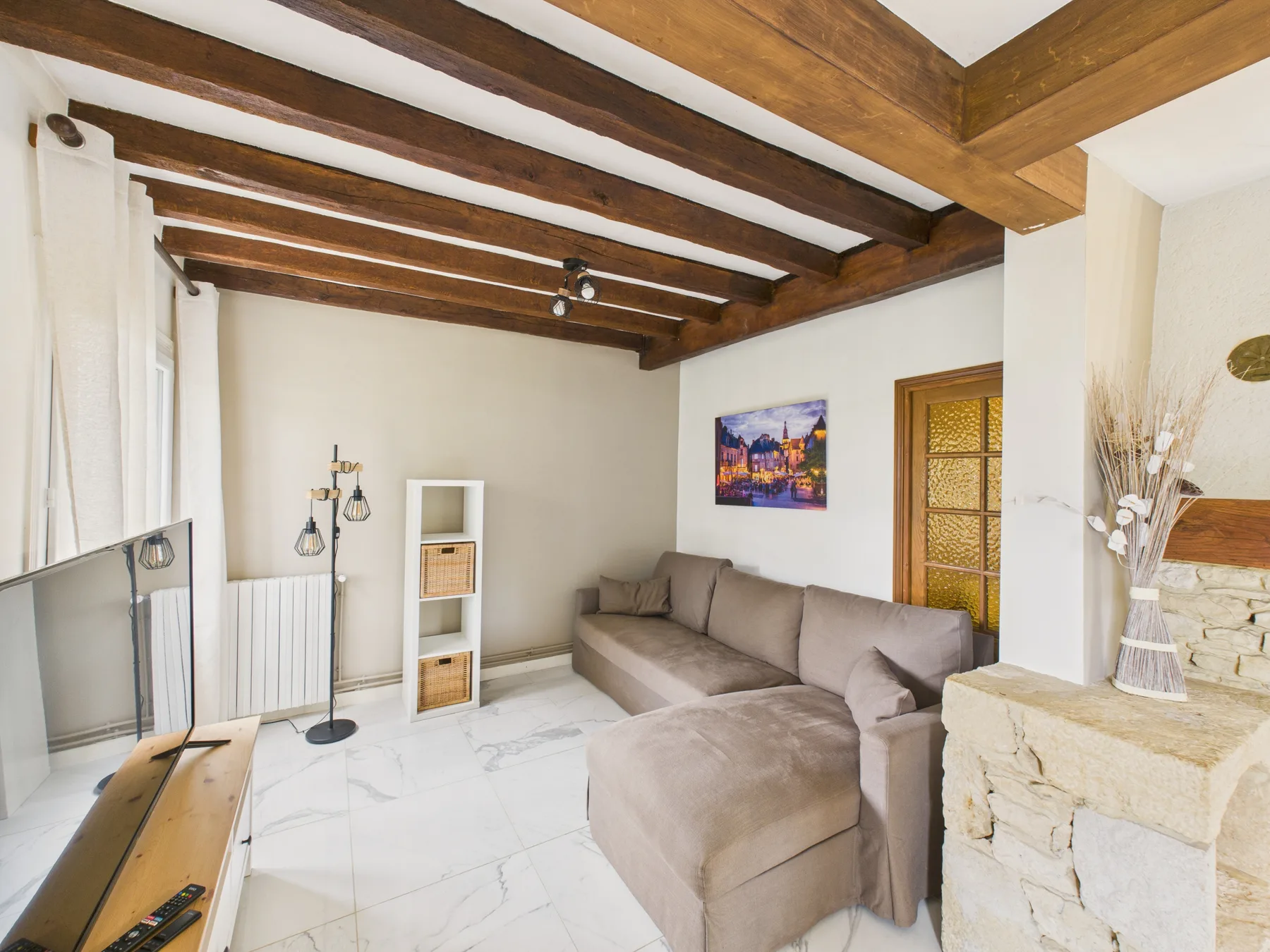 Sala de estar con asientos seccionales, vigas de madera expuestas y un televisor.