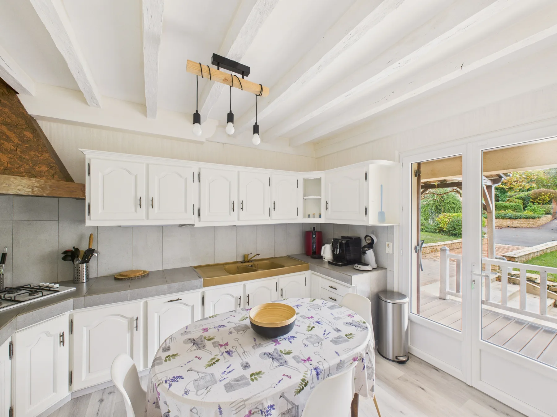 Una cocina luminosa con armarios blancos y una mesa junto a puertas de vidrio.