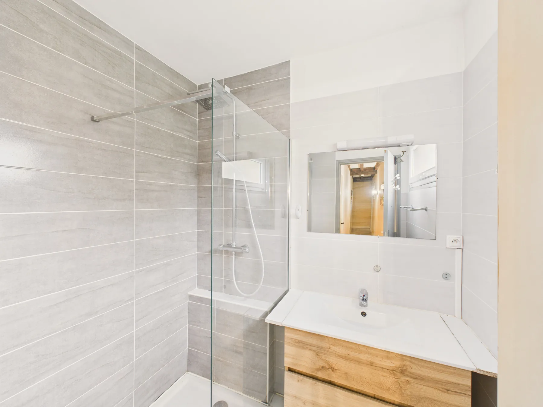 Un baño luminoso con una ducha de vidrio y un lavabo con mueble.
