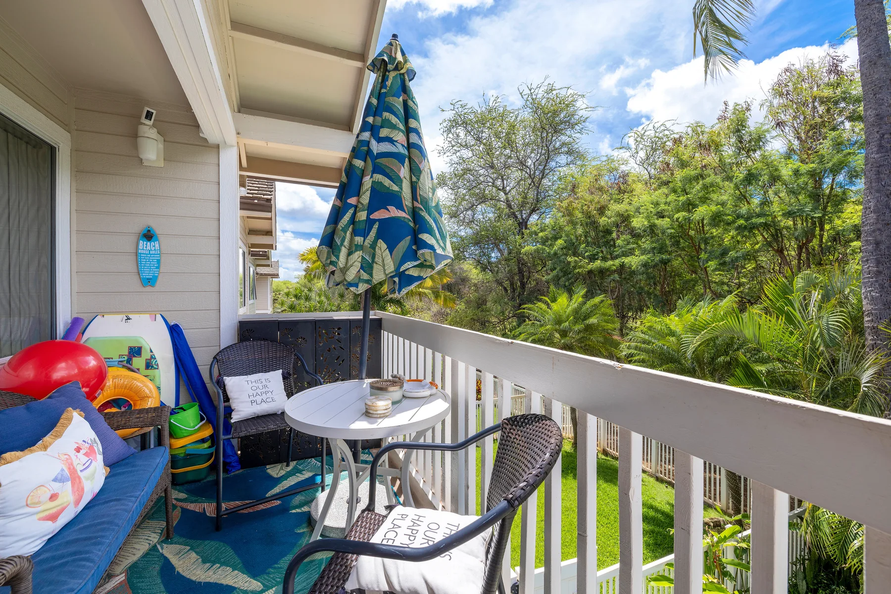 A balcony seating area with a table and a striped umbrella overlooks leafy greenery.