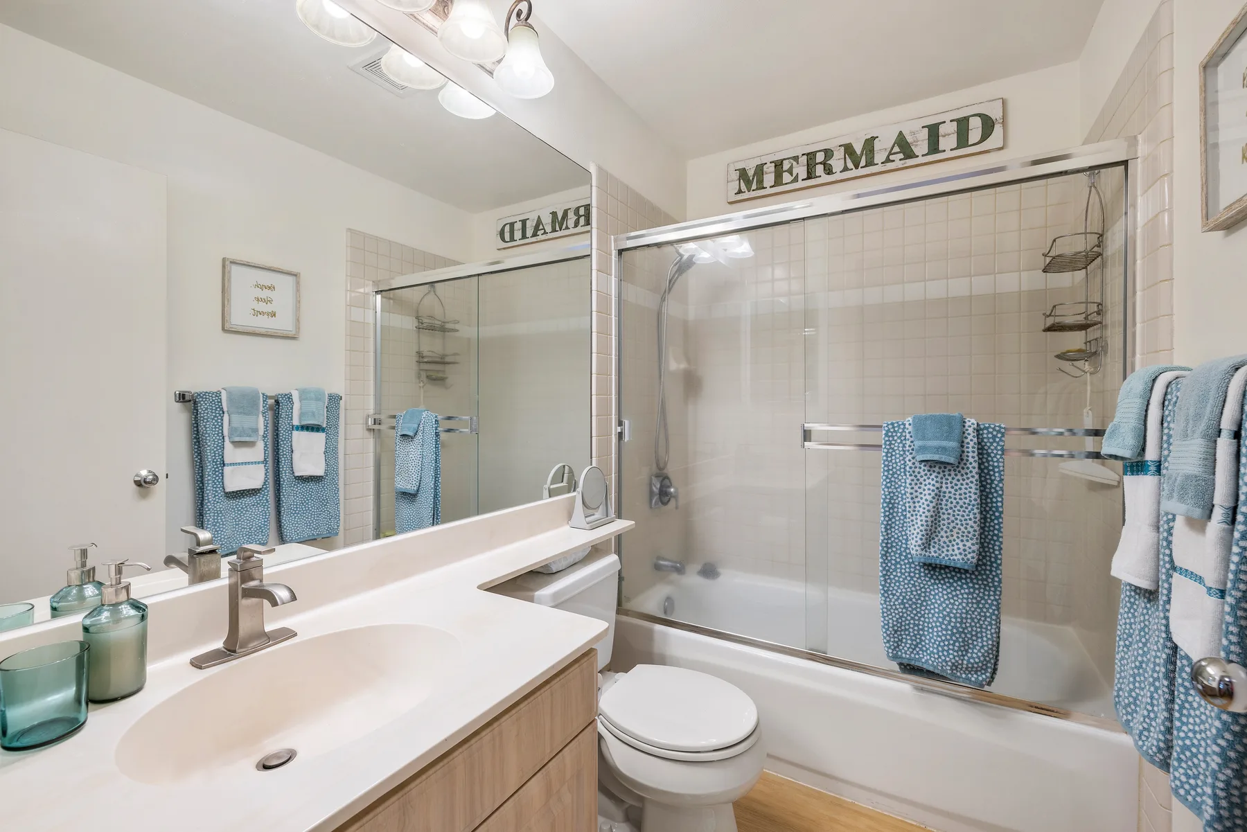 A bright bathroom with a bathtub, glass shower screen, and sink.