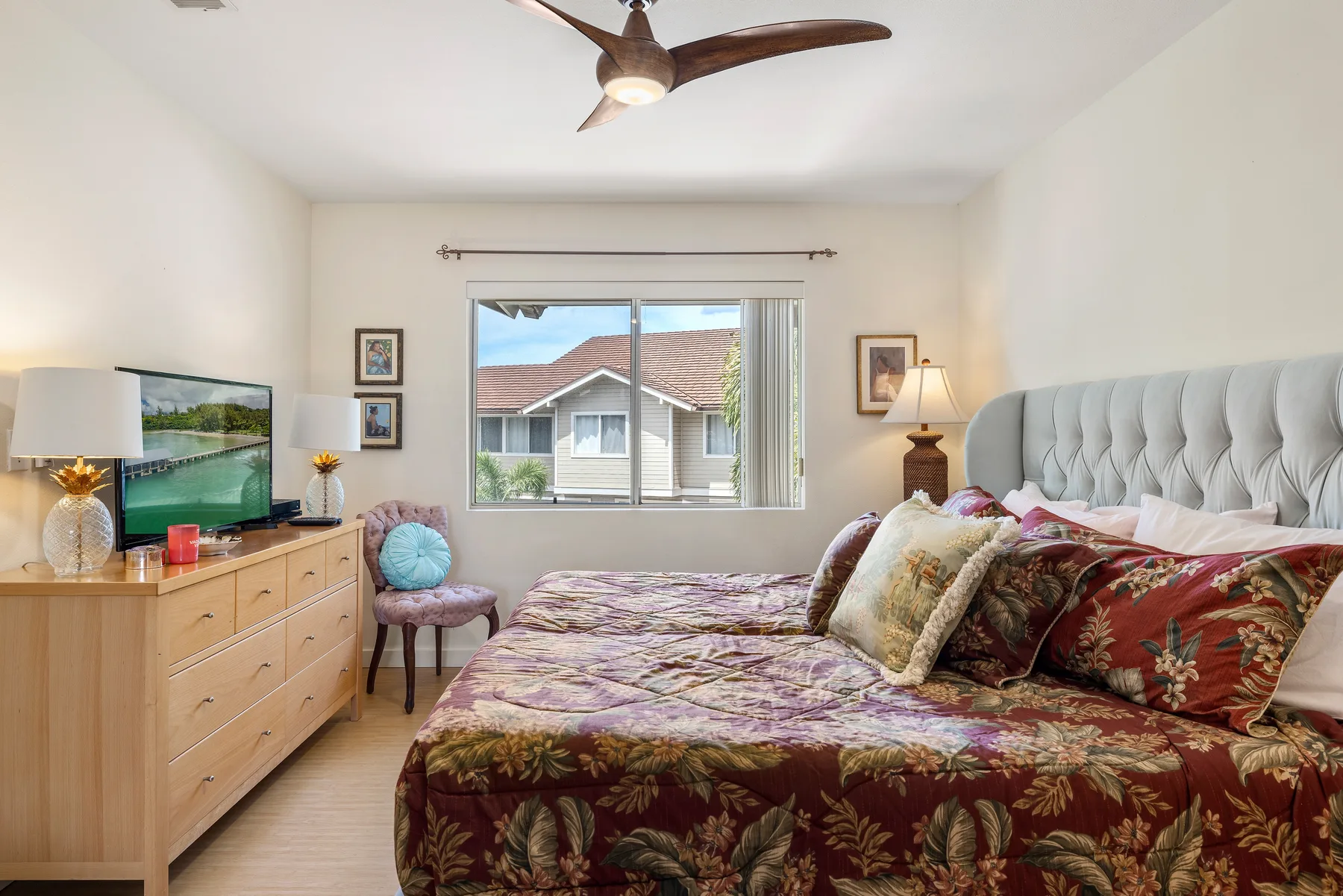A bedroom with a bed, dresser, and window overlooking neighboring houses.