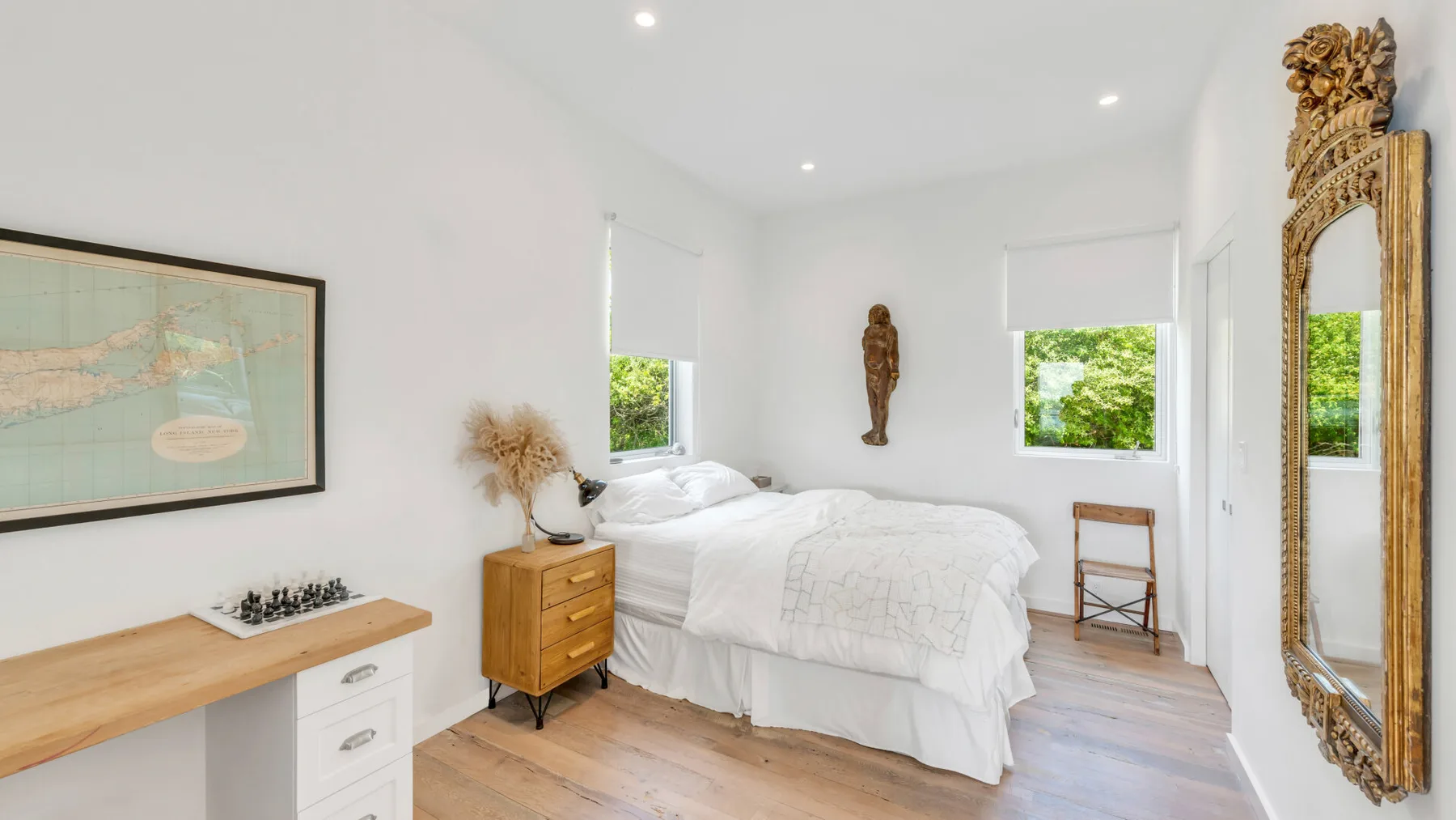 A bright bedroom with a bed, a wooden desk, and windows overlooking greenery.