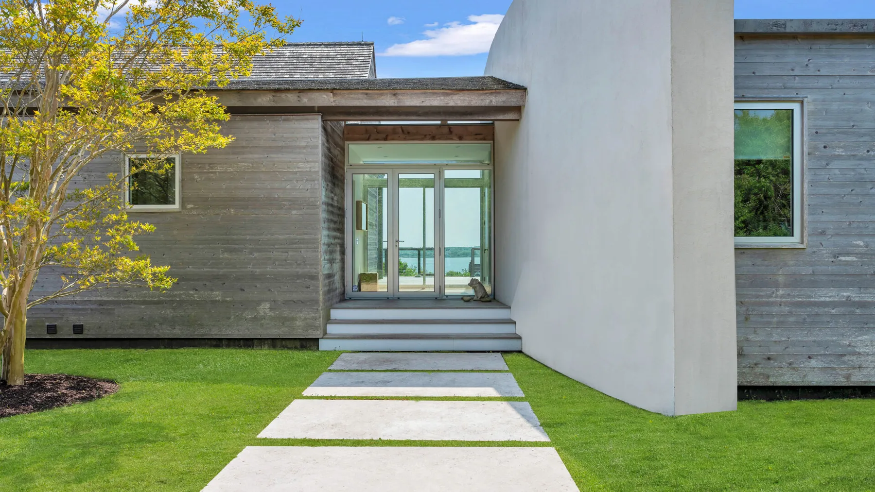 A modern house entrance opens onto a paved walkway through a green lawn.