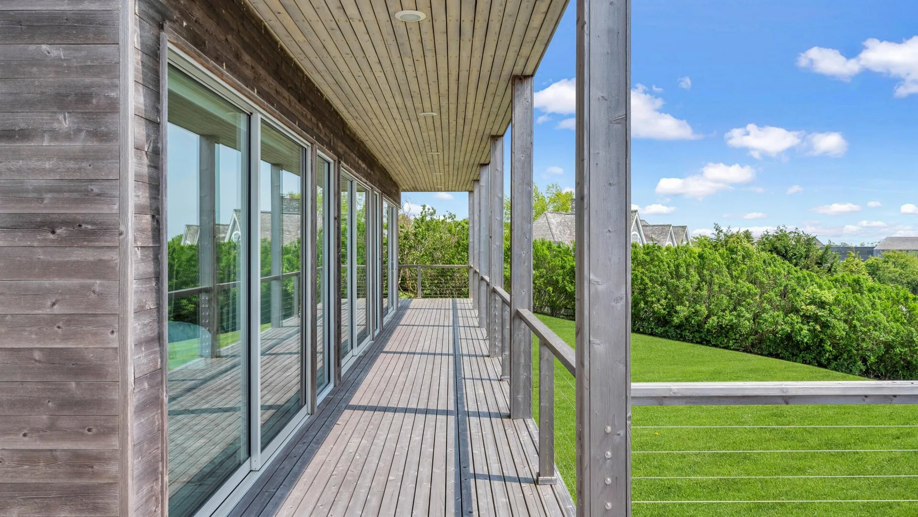 A covered wooden deck runs alongside a building, overlooking green lawns and trees.