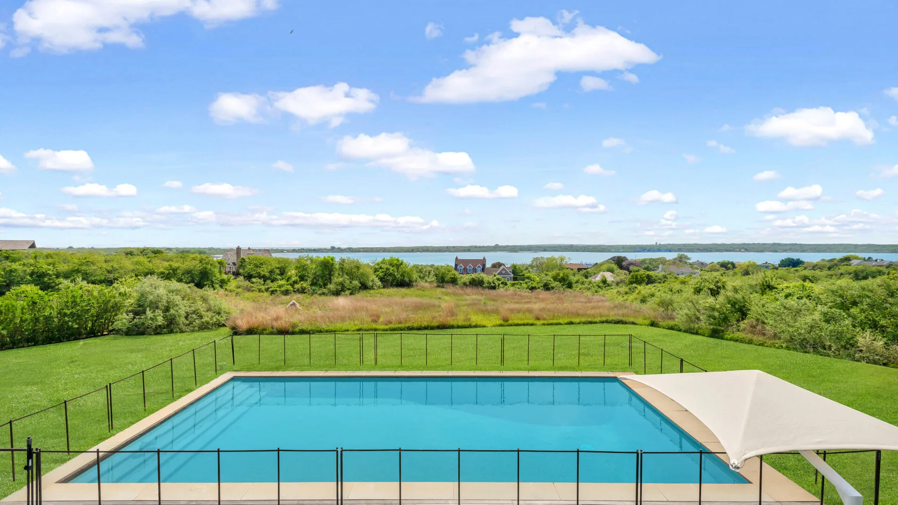 Una piscina al aire libre se encuentra en un paisaje verde cercado.