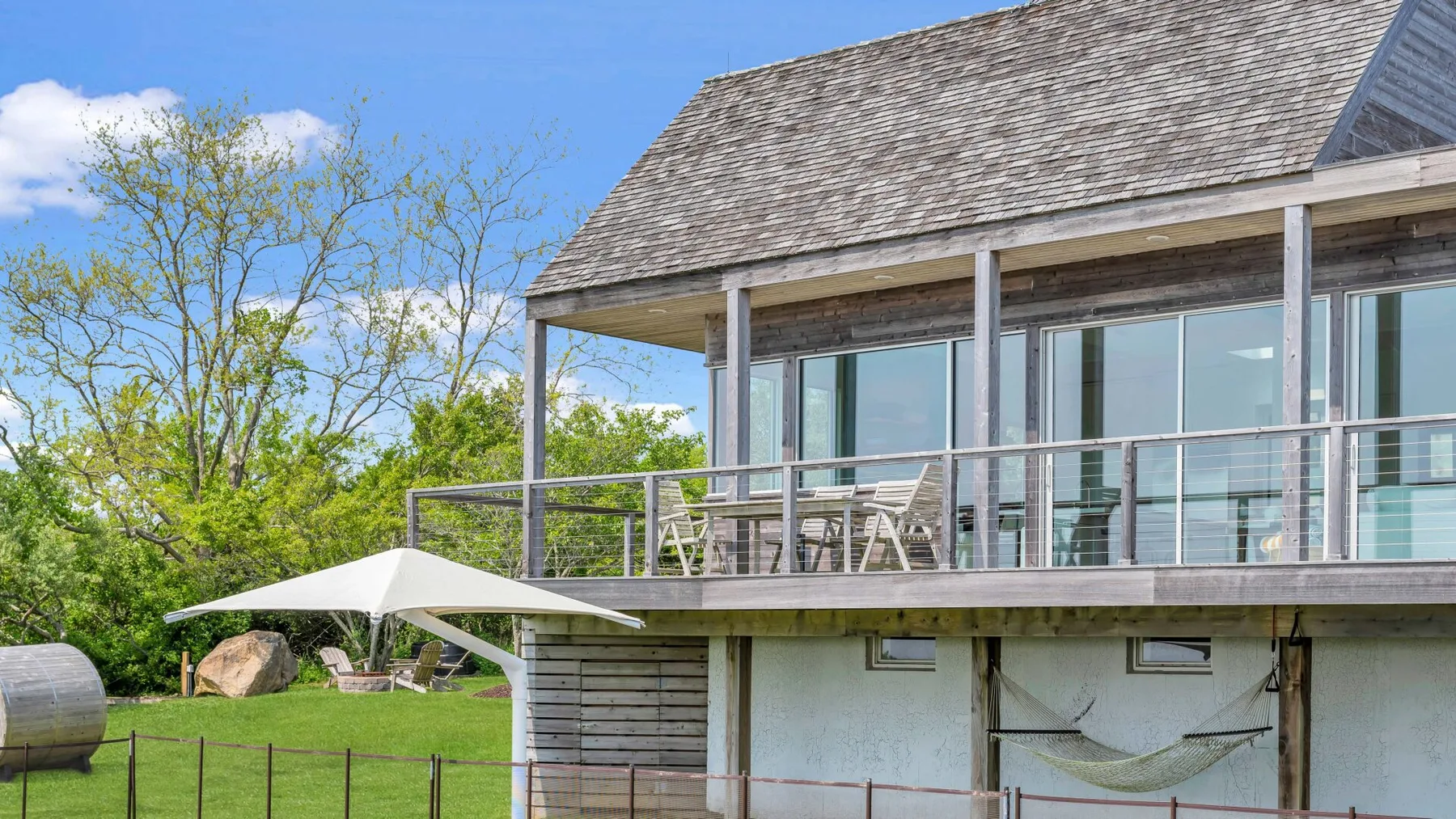 A raised house with a covered balcony and outdoor seating overlooks a green lawn.