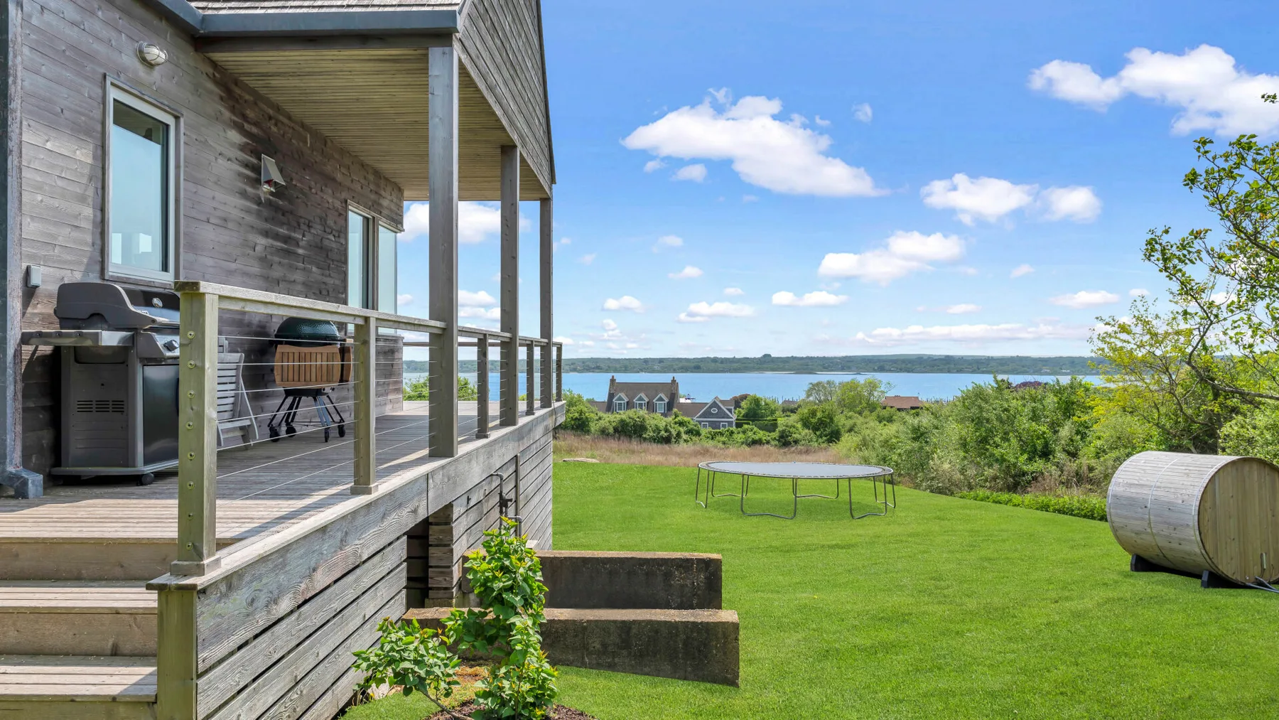 A lakeside lawn beside a wooden deck, with a small trampoline in the grass.