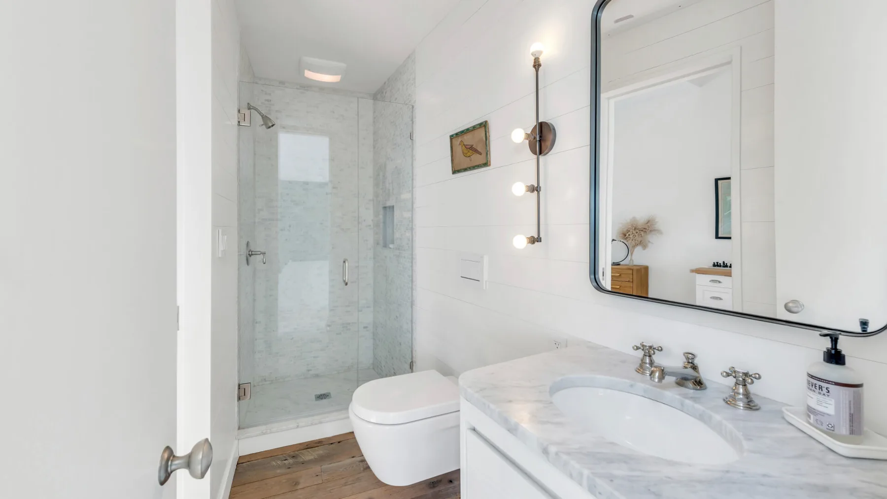 A bright bathroom with a glass shower, toilet, and sink.