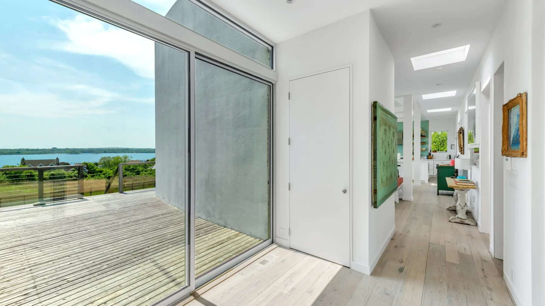 A bright hallway opens onto a deck with wide glass doors and a water view.
