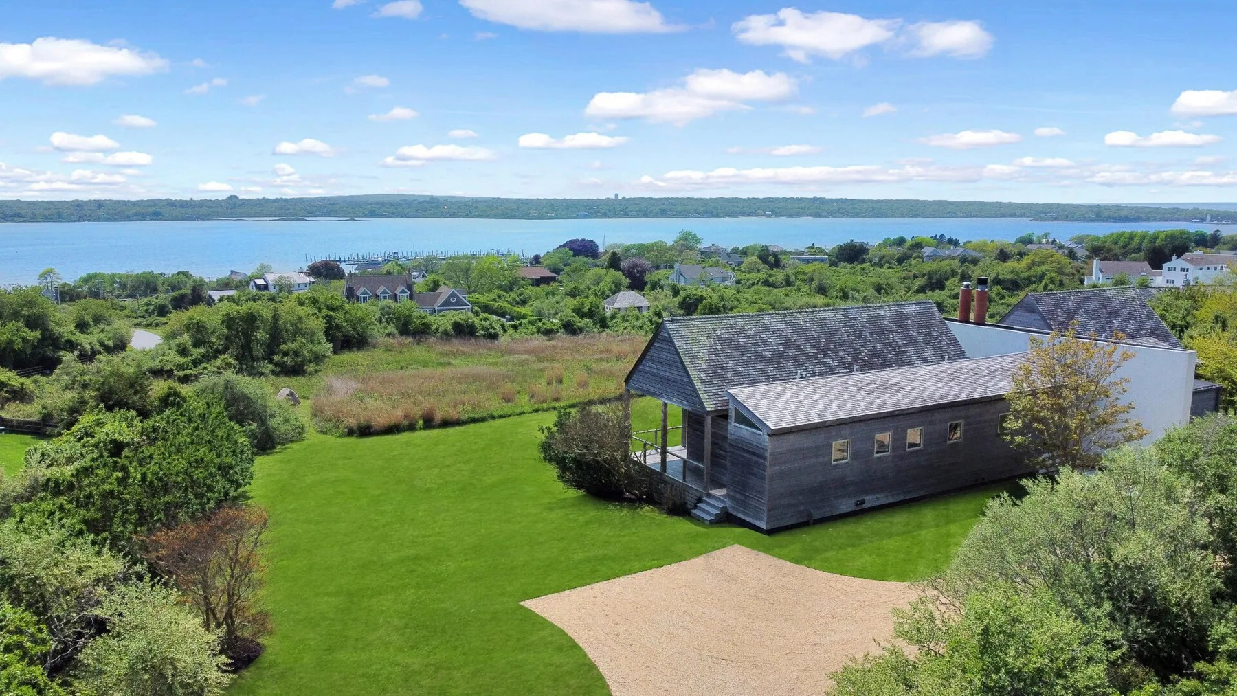 Aerial view of a grassy yard with a wooden building and a lake beyond.