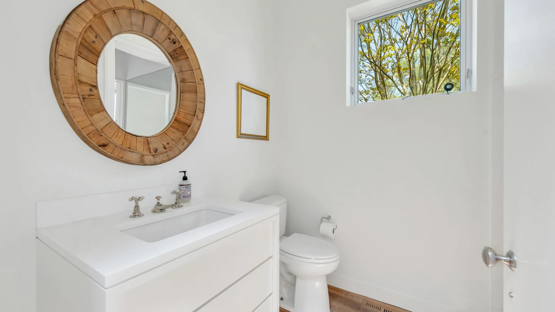 A bright bathroom with a white sink, toilet, and round wall mirror.