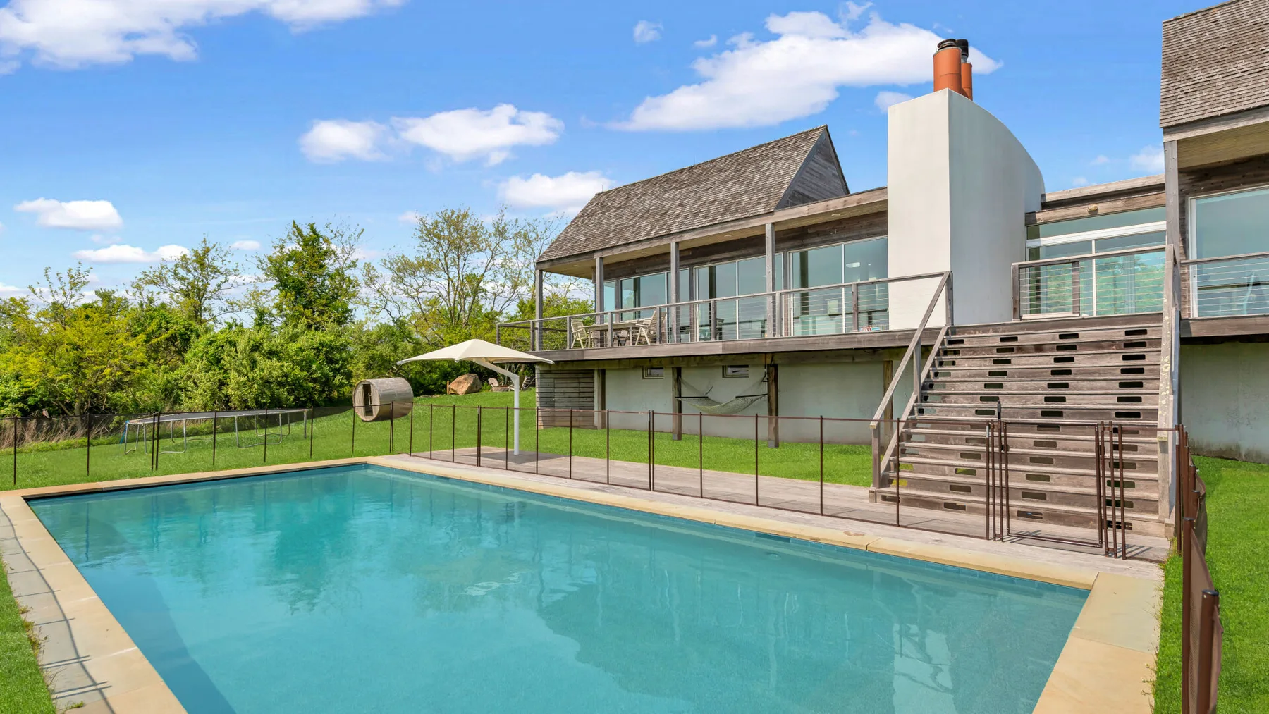 Una piscina está junto a una casa moderna con terraza y escaleras exteriores.