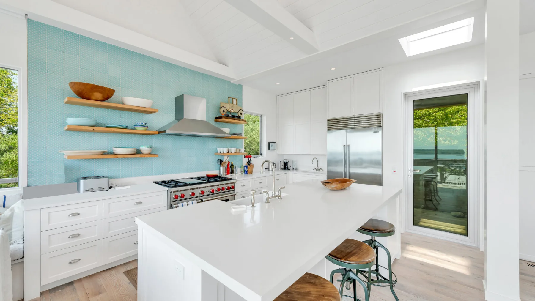 A bright kitchen with a large island, stainless steel appliances, and a turquoise backsplash.