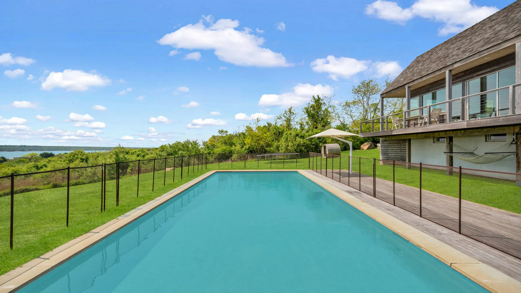 An outdoor swimming pool beside a modern house and green lawn.